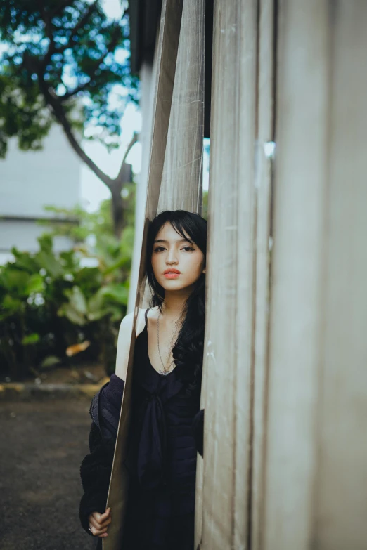 woman wearing black is peeking through a wall