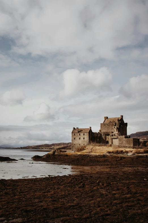 a castle sits next to the ocean on a cloudy day