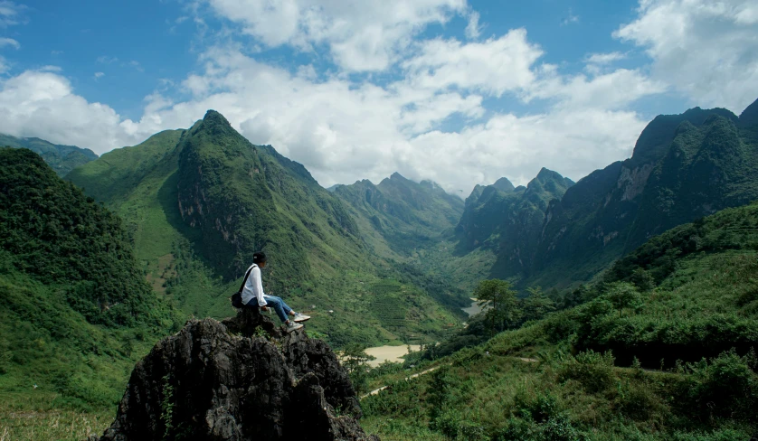 a man is sitting on a cliff in the mountains