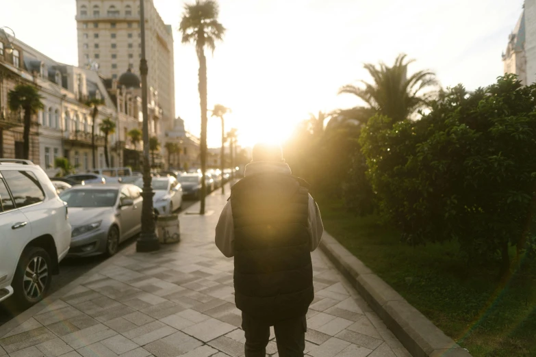 a man with a backpack walks down a city street at sunset