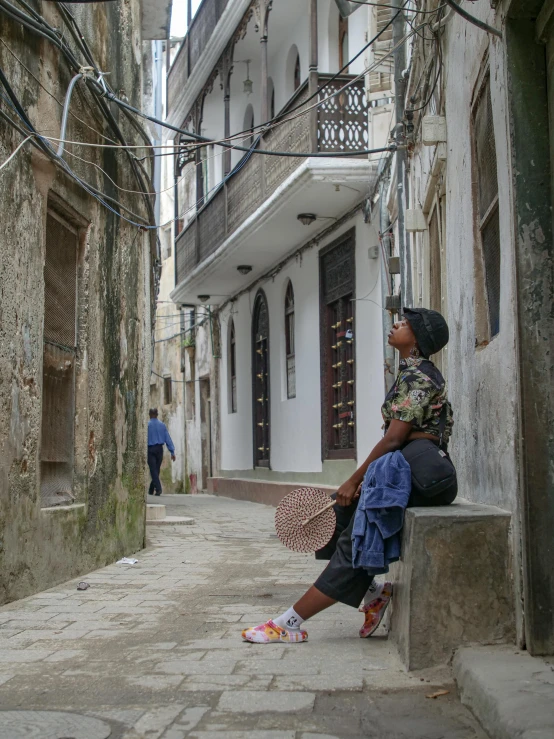 an adult is sitting on a wall looking down a street