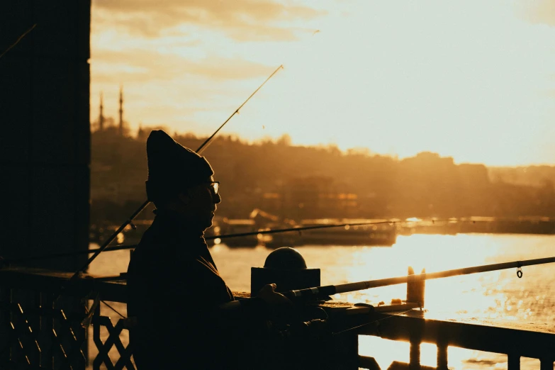 the silhouette of a person sitting at a bench fishing on a river