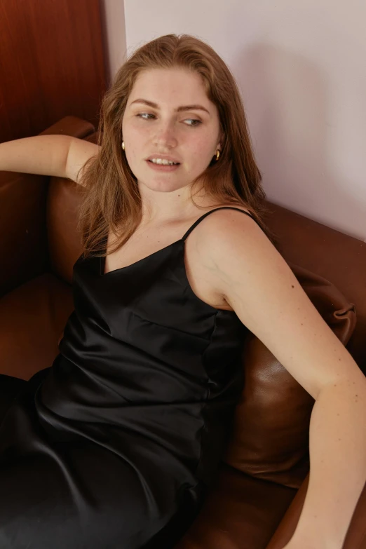 young woman in black satin dress sitting on a brown sofa