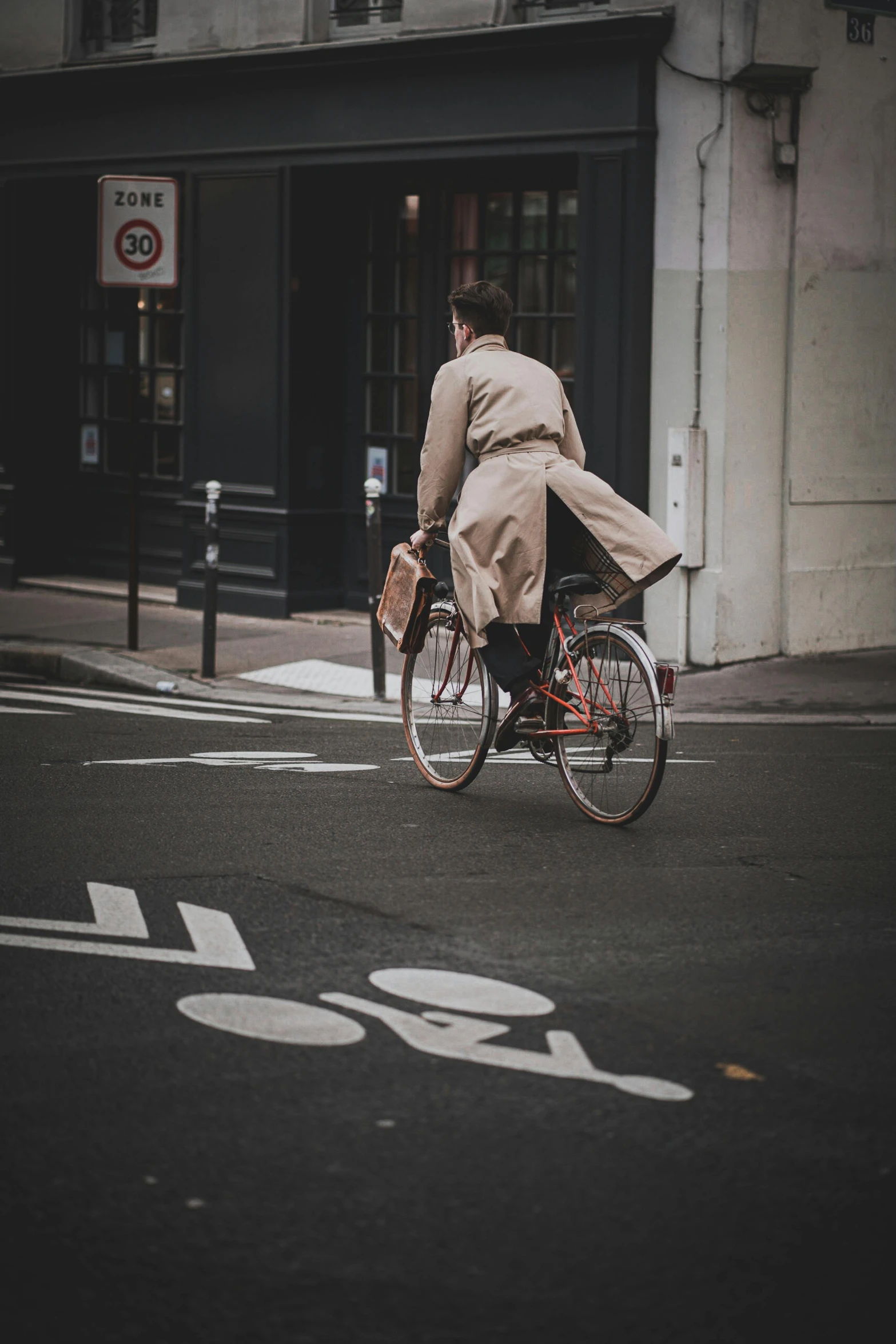 a man in business attire riding his bicycle across the street