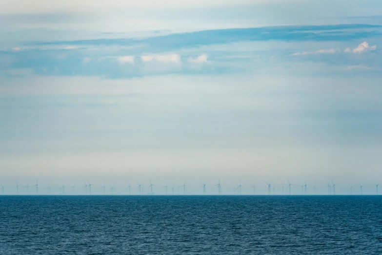 a single boat traveling along the ocean near wind turbines