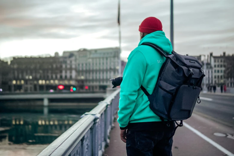 a man walks down the sidewalk next to a bridge with a backpack on his back