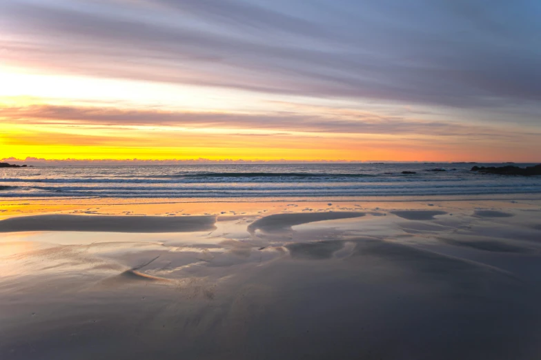 a wave hitting the beach during sunset with the sky in the background