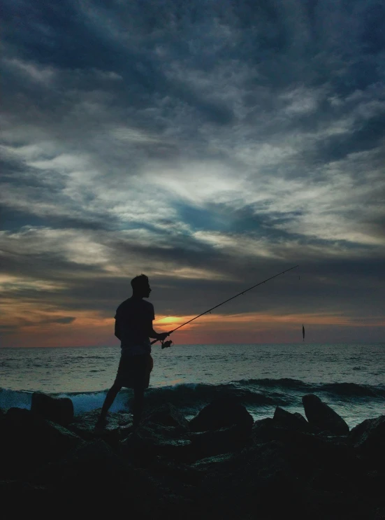 a man fishing in the distance at sunset