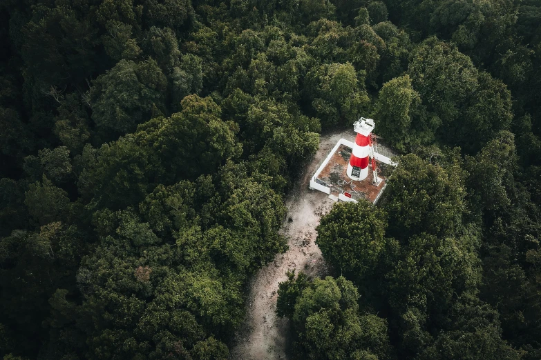 an aerial view shows the red lighthouse and path through a forested area