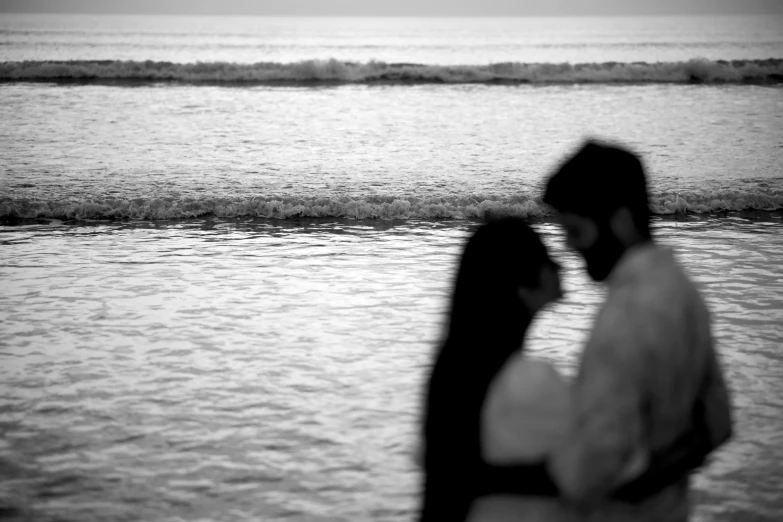 man and woman holding each other in their arms near the ocean