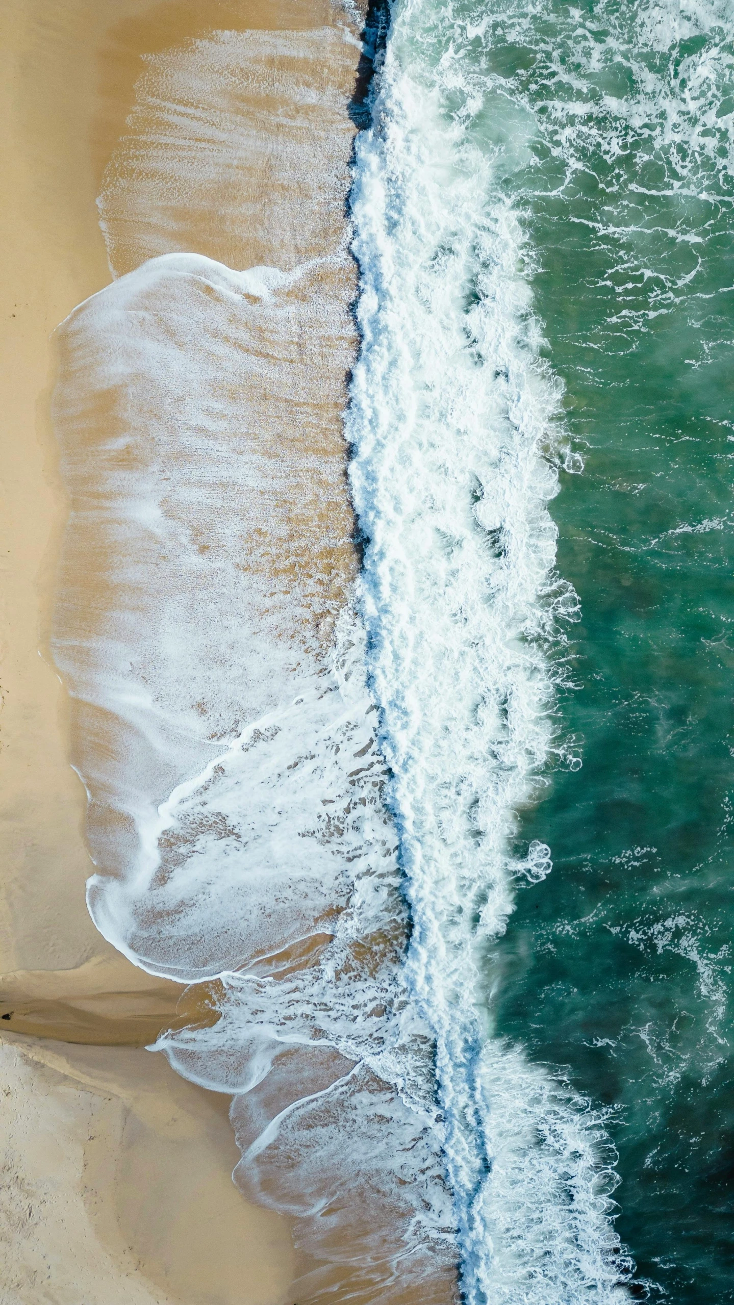 an aerial view of the ocean and waves on a sandy beach