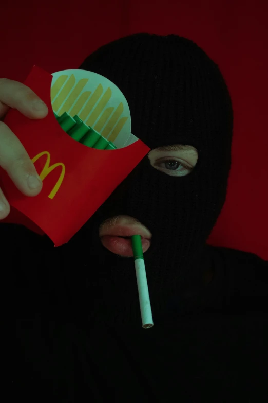 the woman has her face covered as she smokes a cigarette and eats mcdonald's fries