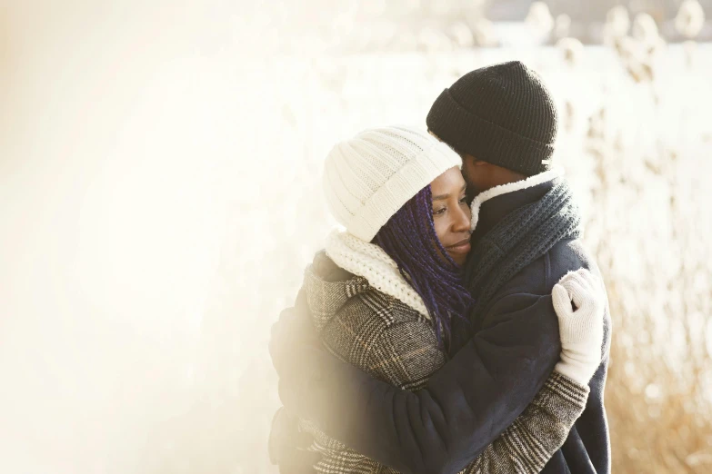 man and woman hug while standing in front of snowy trees