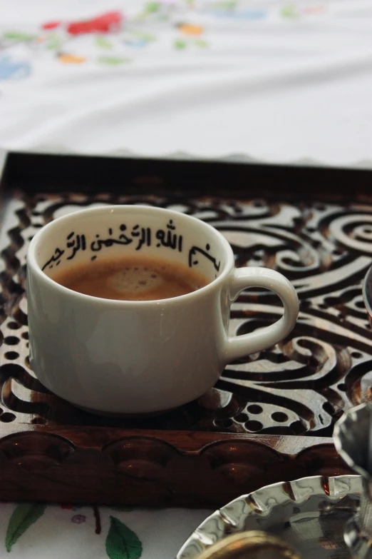 the white cup with arabic writing is beside a spoon