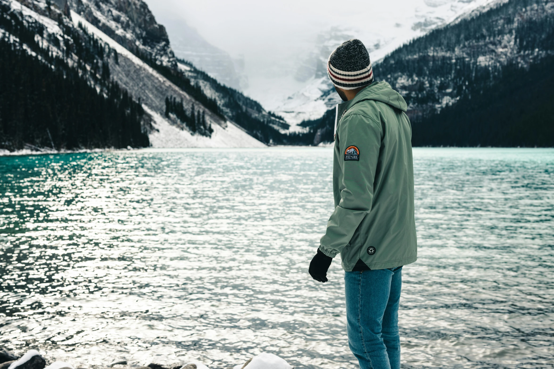 a man is standing near the water looking at the mountain