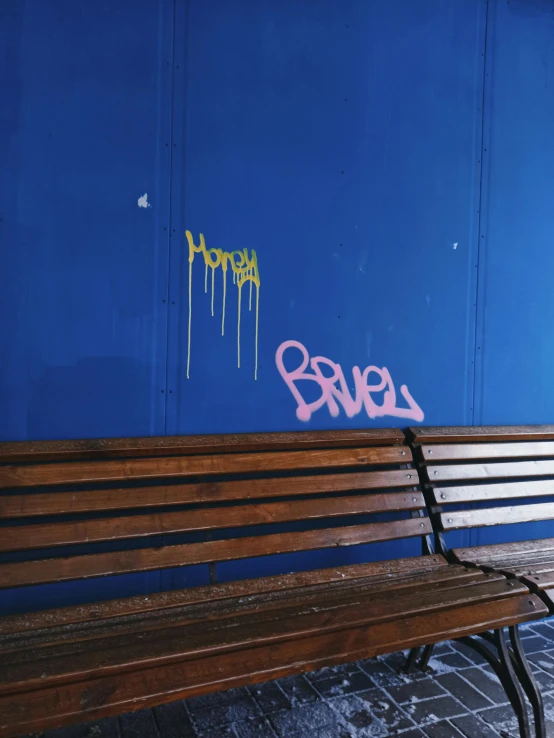 a bench is covered with graffiti and in front of a blue wall