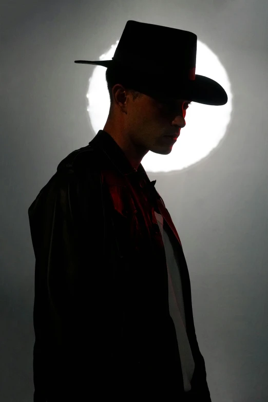 a man wearing a hat stands against a circular light