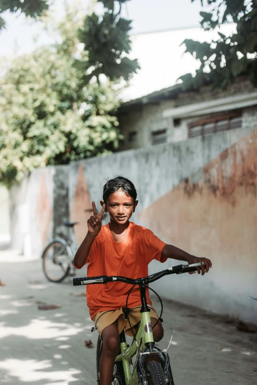 boy sitting on green bicycle giving peace sign