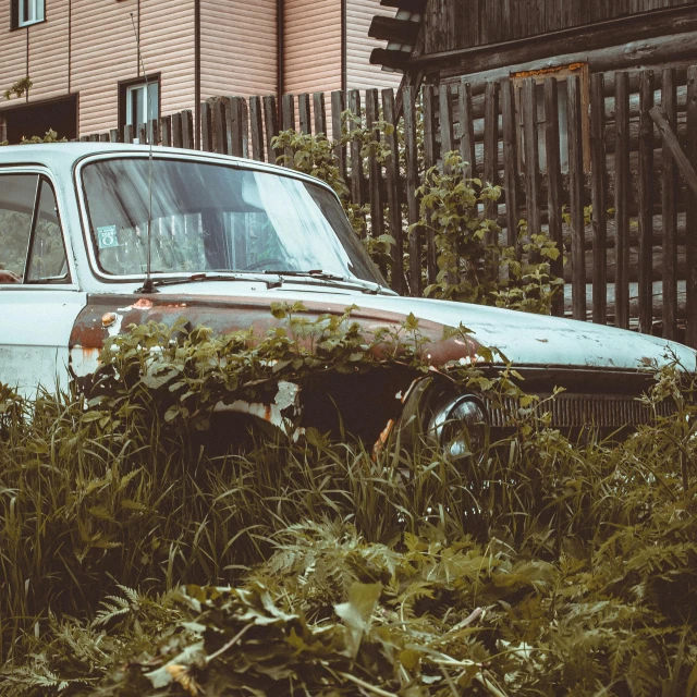 an old rusted car parked in the middle of some weeds