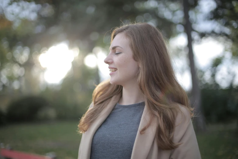 woman standing with eyes closed near bench and trees