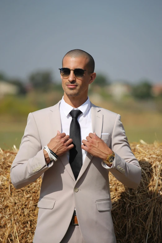 a man in a suit adjusts his tie while standing next to hay bales