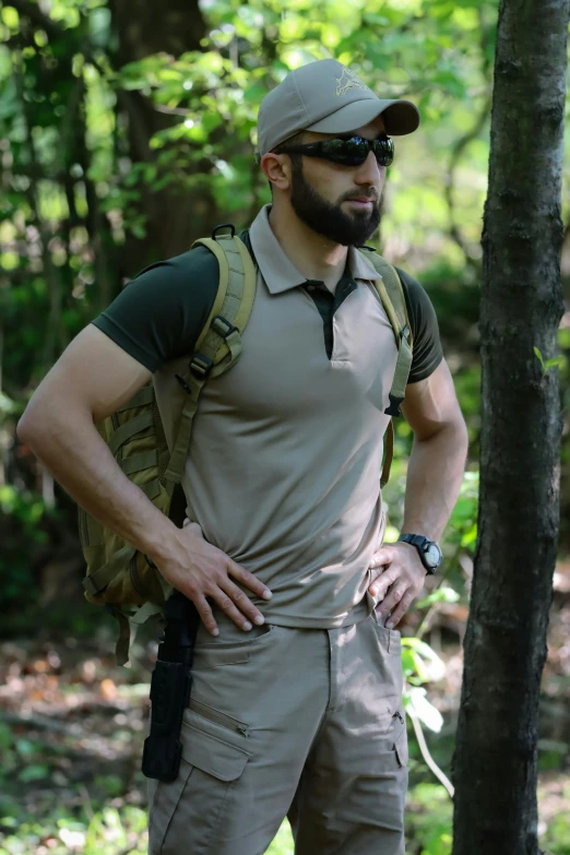 a man with a beard in a military outfit stands next to a tree