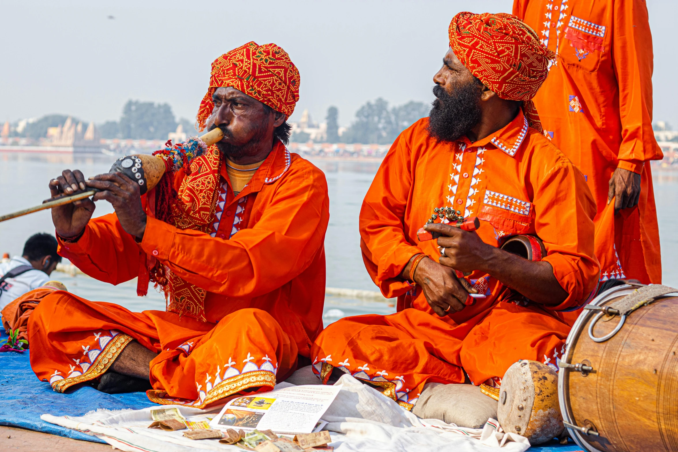 two men sit on a towel playing music together