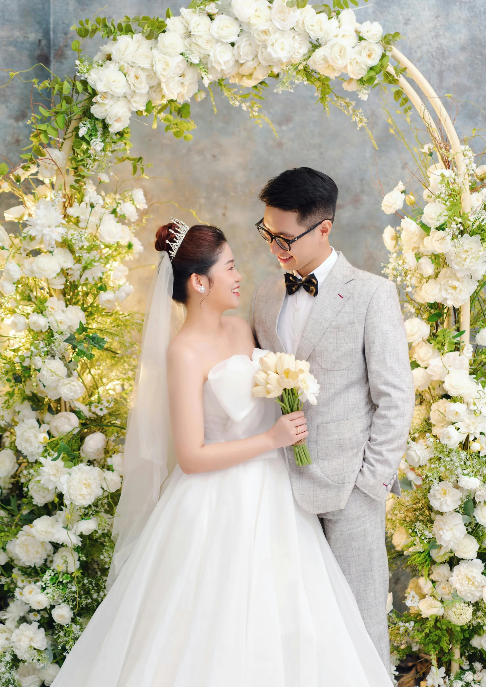 bride and groom posing in front of a white arch and flower decor