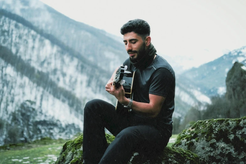 a man in black holds his camera while sitting on a rock