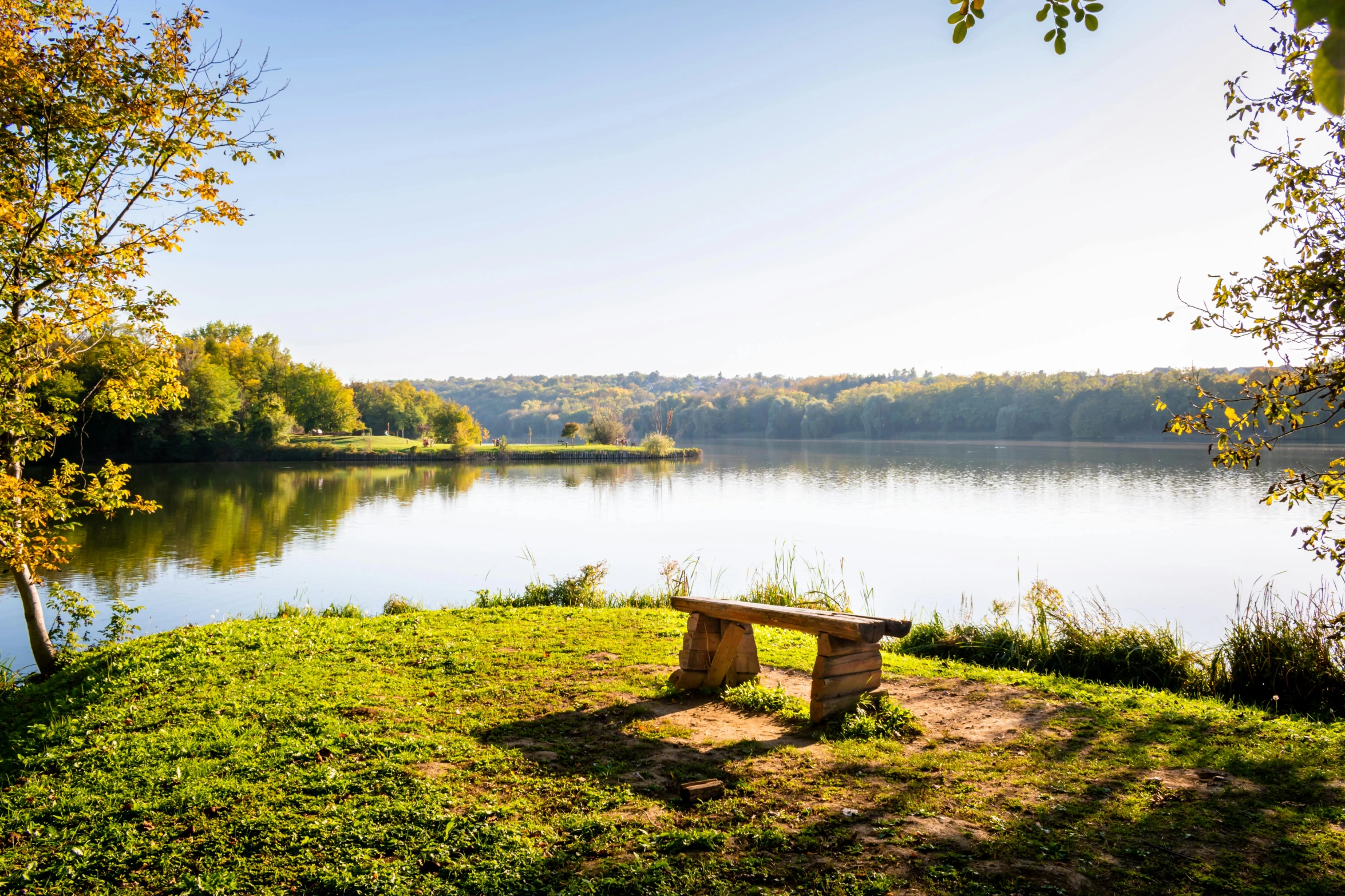 a park bench on the shore of a lake in autumn