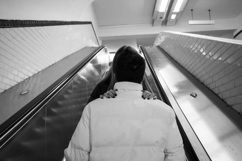 black and white pograph of woman wearing coat on escalator
