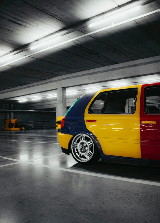 the small yellow, red, and blue compact car is parked in a garage