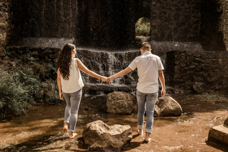 an engaged couple walking through a water fall