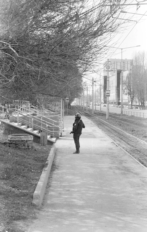 black and white pograph of person walking on sidewalk by railroad tracks