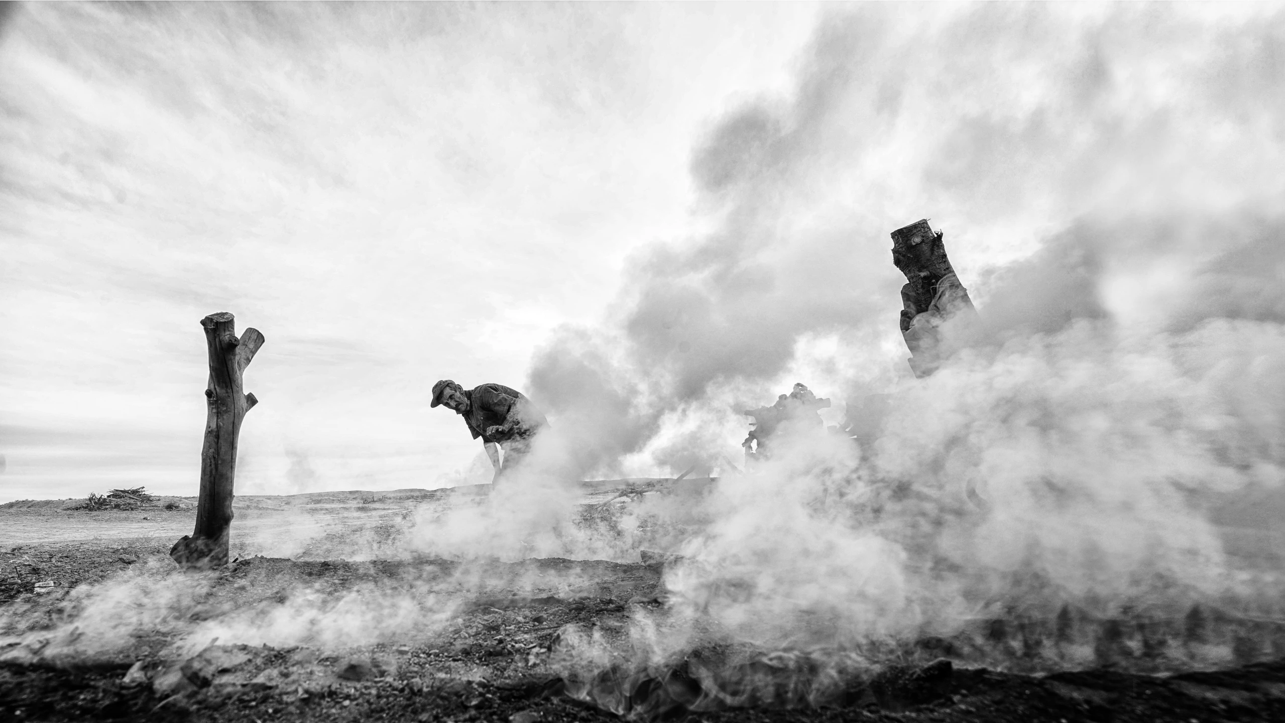 smoke rising from an open field near a wooden post