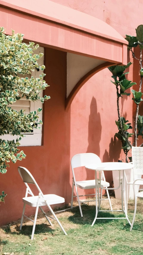 a red wall with a couple of white chairs and some trees