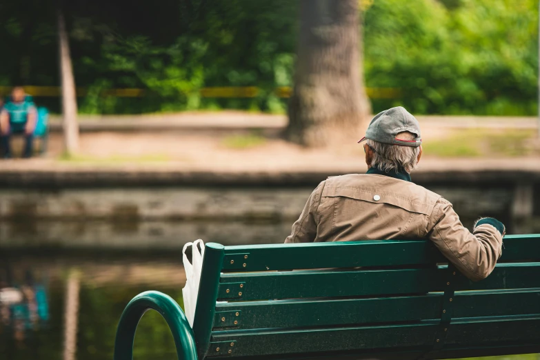 an old man sitting on a green bench looking out into the lake