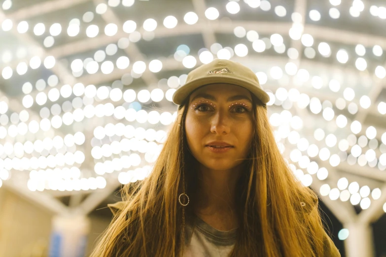 a woman with long hair and a cap in front of a lot of lights