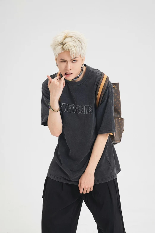 a young man with blond hair is wearing black clothing and holding a brown handbag