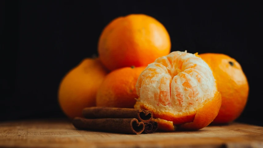 oranges are piled on top of each other with cinnamon sticks and an apple in front