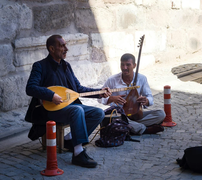 two guys sitting on the sidewalk playing music