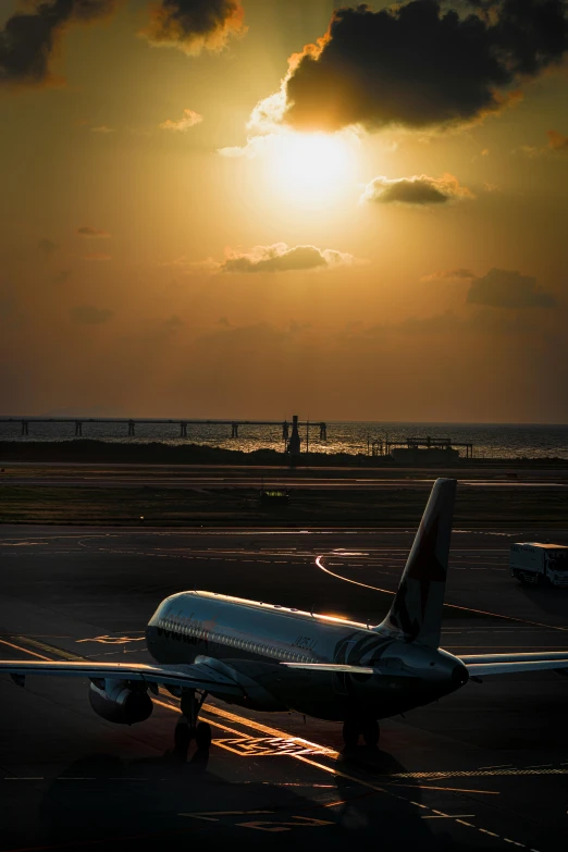 an airplane parked on the runway with clouds and sun shining