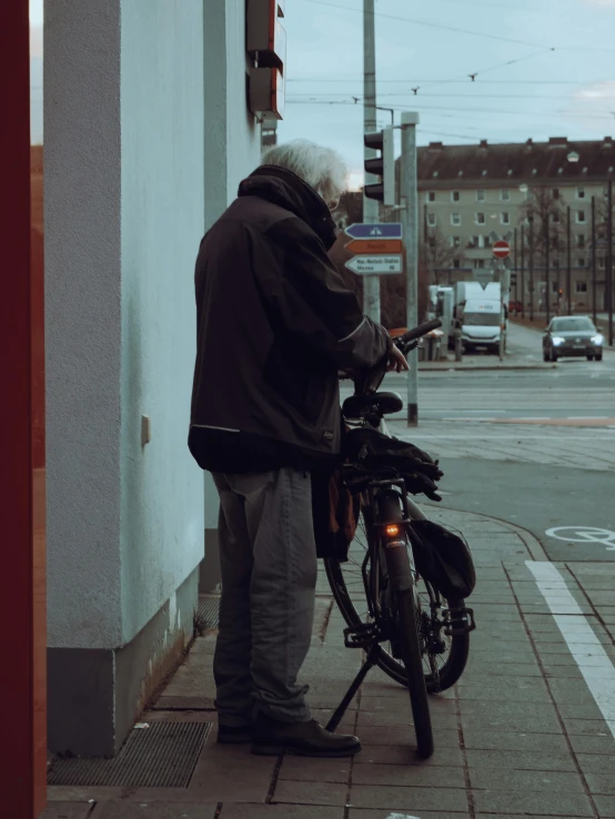 an old man on a bike reads soing while standing next to the street