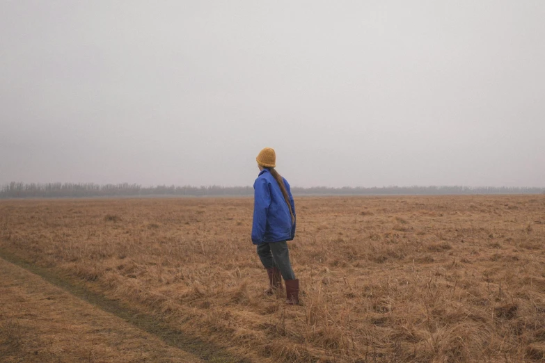 a person in a blue jacket is standing in a large open field