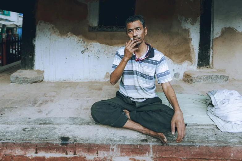 a man in striped shirt sitting on concrete and smoke