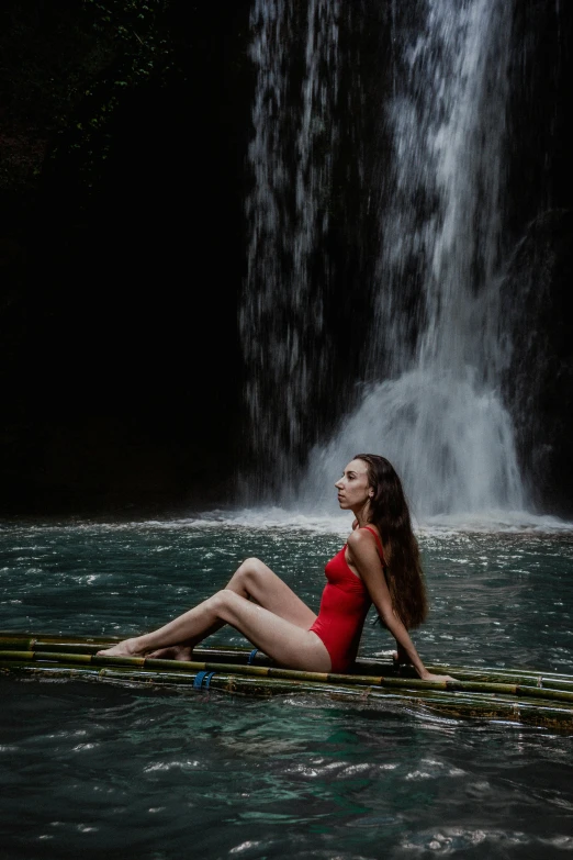 the beautiful woman is sitting in the water next to a waterfall