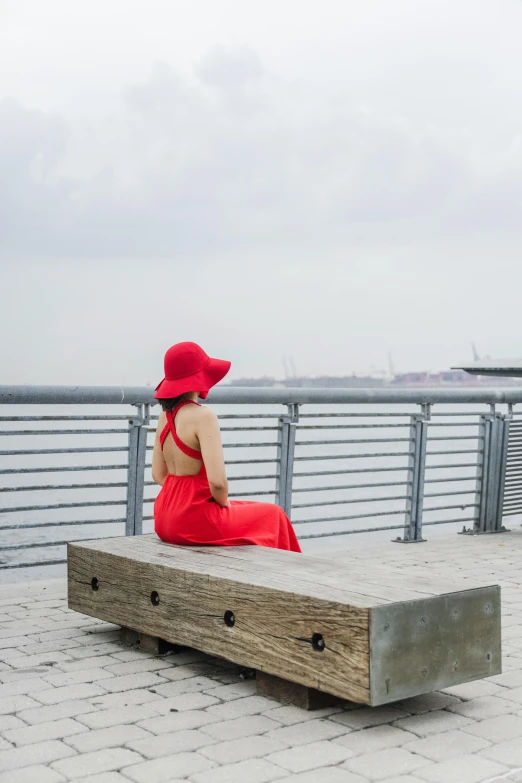 woman in red dress and hat sitting on large wooden bench