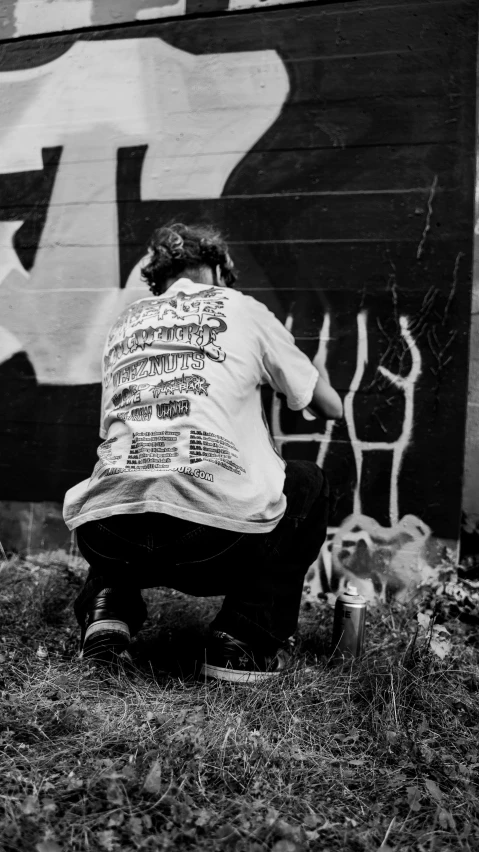 woman is sitting on the grass with cans in front of a wall that has been painted with graffiti