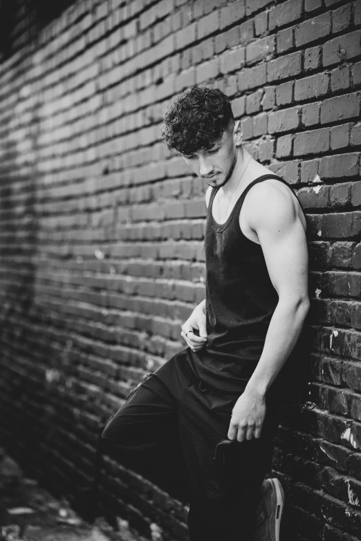 a man leaning against a brick wall looking at his phone