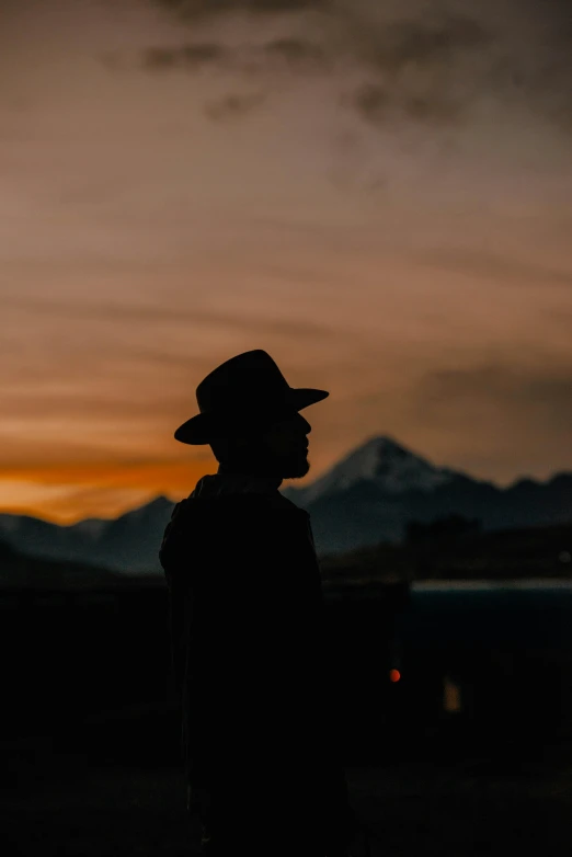 silhouetted person standing at sunset with mountains in background